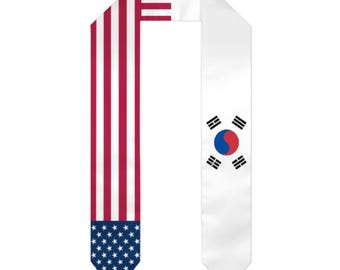 May include: A white graduation sash featuring the flags of the United States and South Korea. The left side displays the American flag with red and white stripes and blue stars. The right side shows the South Korean flag.