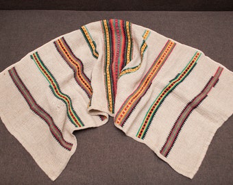 Puede incluir: Una tela blanca tejida con rayas de colores en rojo, amarillo, verde y negro. La tela está doblada por la mitad y tiene una superficie texturizada.