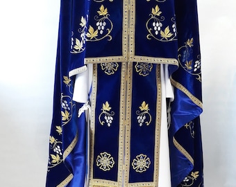 May include: A blue velvet liturgical vestment with gold and white embroidery. The vestment features a grapevine design and is worn by a priest during religious ceremonies.