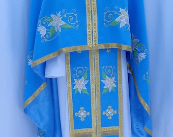 May include: A blue liturgical vestment with white floral embroidery and gold trim. The vestment has a long, flowing robe with a white undergarment and a matching stole.
