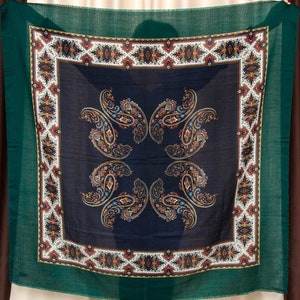 Peut inclure: Un foulard carré avec un motif paisley dans des tons de bleu, vert et marron. Le foulard a une bordure vert foncé et une bordure intérieure blanche et rouge.
