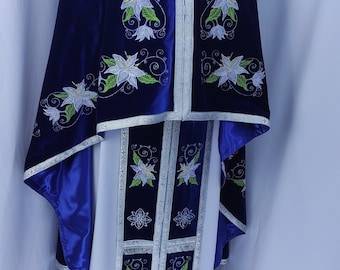 May include: A blue and white liturgical vestment with floral embroidery. The vestment has a long white robe with a blue velvet trim and a matching blue velvet cape with floral embroidery.