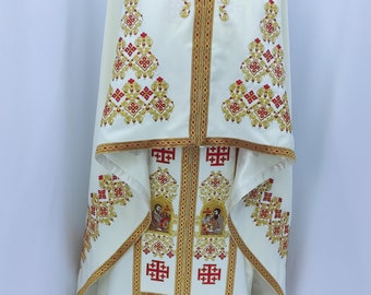 Könnte beinhalten: Weißes liturgisches Gewand mit goldener und roter Stickerei. Das Gewand besteht aus einer langen Robe mit einem dekorativen Kragen und einer passenden Kapuze. Die Stickerei umfasst komplizierte florale Muster und religiöse Symbole.