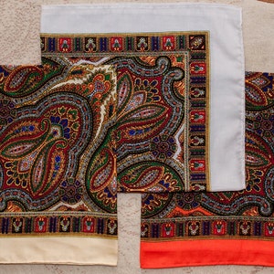 以下が含まれることがあります： 白、クリーム、オレンジの3枚のペイズリー柄のスカーフ。スカーフは、カラフルなペイズリー柄で、黒い縁取りがされています。