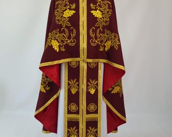 May include: A burgundy religious garment with gold embroidery featuring floral and grape vine designs. The garment has gold trim and red lining, displayed on a black mannequin head. The garment is a long robe with a matching cape.