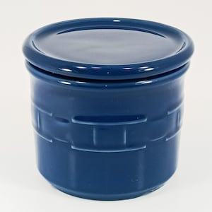 May include: A cobalt blue ceramic jar with a matching lid. The jar has a cylindrical shape with a textured, basketweave-like pattern around the body. The lid sits flush on top, creating a clean, cohesive look. The glossy finish reflects light.