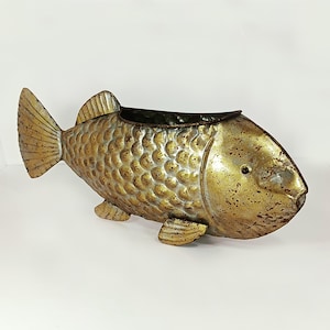 May include: A decorative metal fish planter with a distressed gold finish. The fish-shaped container has a dark interior and is designed with scales, fins, and a tail. The planter is approximately 18 inches long.