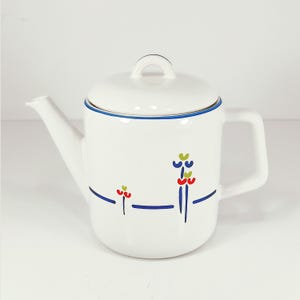 May include: White ceramic teapot with a lid and handle. The teapot has a blue rim and is decorated with blue lines and colorful floral designs in red, green, and yellow. The spout is on the left side.
