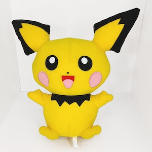 May include: A plush Pikachu doll in bright yellow with black-tipped ears and a black collar. The doll has pink cheeks, a red tongue, and large black eyes. It is a soft, cuddly toy.