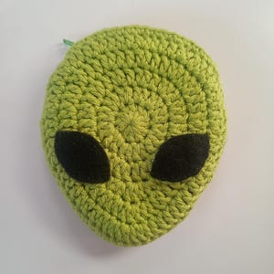 May include: A handmade, lime green crocheted alien face with large black oval eyes. The alien head is round and has a small green loop at the top. The background is plain white.