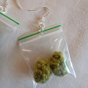 May include: Novelty earrings with crocheted green buds inside clear plastic bags with green zip closures. The earrings have silver-coloured fish hook ear wires.