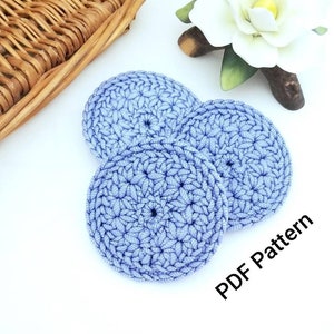 May include: Three crocheted lavender blue round coasters. The coasters are made with a textured stitch pattern. The text "PDF Pattern" is visible in the image.