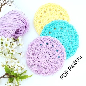 May include: Three crocheted coasters in pastel colors: lavender, turquoise, and yellow. The coasters have a circular design with a center hole. The text "PDF Pattern" is visible in the lower right corner of the image.
