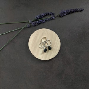 Peut inclure: Trois anneaux en argent et deux boucles d'oreilles carrées noires sur un plateau en bois avec une brindille de lavande.
