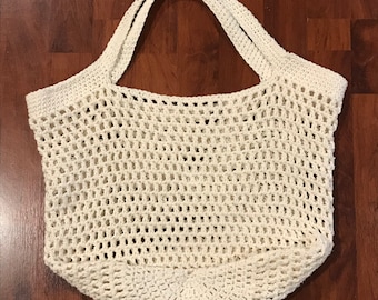 May include: A white crocheted tote bag with a wide, open top and two thick handles. The bag is made of a simple, open weave pattern.