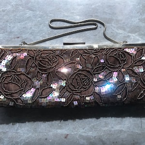 May include: A brown sequined clutch bag with a silver chain strap. The bag is decorated with a floral pattern and iridescent sequins.