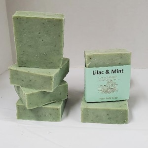 May include: A stack of five green goat milk soap bars. The top bar has a label that reads "Lilac & Mint Goat Milk Soap".