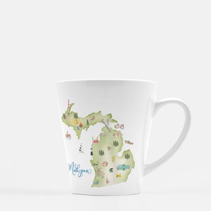 Puede incluir: Taza de cerámica blanca con una ilustración en acuarela del estado de Michigan. El diseño incluye puntos de referencia y la palabra "Michigan" en escritura cursiva. La taza tiene un asa curva y una forma cónica.