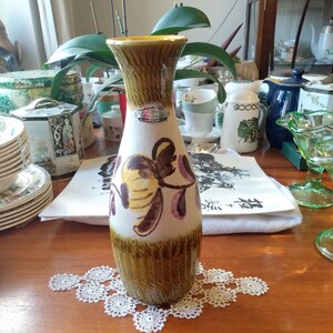 May include: A brown and white ceramic vase with a yellow, pink, and brown floral design. The vase has a textured, ribbed surface and a label that reads "Bavaria Handarbeit".
