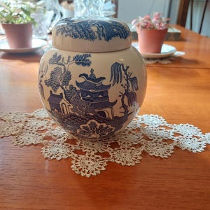 May include: A white ceramic jar with a blue and white willow pattern. The jar has a lid and is decorated with a traditional Chinese design.
