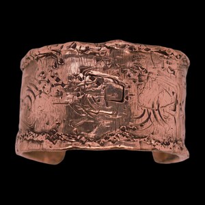May include: A wide copper cuff bracelet featuring a heavily textured, rugged surface with deep grooves, irregular indentations, and a metallic reddish-brown finish. The edges are uneven and jagged, creating a raw, organic appearance across the band.