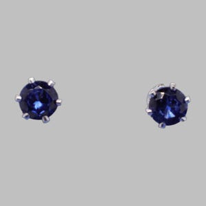 May include: A pair of round-cut, deep blue sapphire stud earrings set in silver-toned metal prongs. Each earring features a faceted gemstone with a brilliant sparkle, secured by a six-prong setting that holds the stone firmly in place.