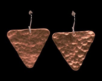 May include: A pair of copper-colored earrings featuring a hammered, triangular design. Each earring is suspended from a silver-toned metal hook, showcasing a textured surface with numerous small indentations across the entire triangular shape.