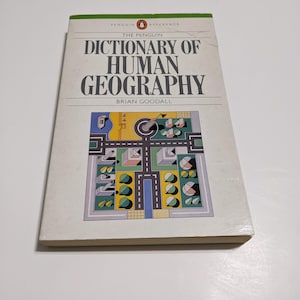May include: A Penguin Reference book titled "The Penguin Dictionary of Human Geography" by Brian Goodall. The cover features a colorful illustration of a city with buildings, streets, and trees.