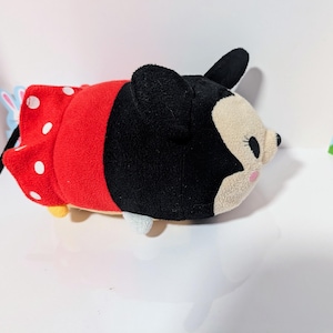 Peut inclure: Un jouet en peluche de Minnie Mouse portant une robe rouge &agrave; pois blancs. Le jouet est couch&eacute; sur le c&ocirc;t&eacute;, la t&ecirc;te tourn&eacute;e vers la droite. Le jouet a des oreilles noires et un nez noir.