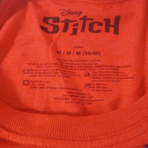 Puede incluir: Camiseta roja con un gr&aacute;fico azul de Stitch e instrucciones de cuidado en la parte posterior. La etiqueta dice "Disney Stitch" y "M/M/M (38/40)".