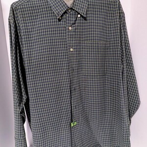 May include: A long-sleeved button-down shirt in a plaid pattern of navy blue, olive green, and light yellow. The shirt has a button-down collar, a chest pocket, and a tag that reads "Haggar".