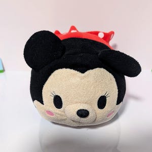 Peut inclure: Un jouet en peluche de Mickey Mouse portant une robe rouge &agrave; pois blancs. Le jouet est rond et a un visage souriant avec des yeux noirs et un nez noir.