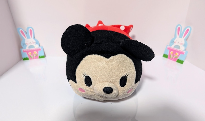 Peut inclure: Un jouet en peluche de Mickey Mouse portant une robe rouge &agrave; pois blancs. Le jouet est rond et a un visage souriant avec des yeux noirs et un nez noir.