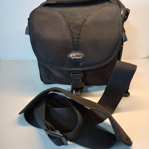 May include: Black camera bag with an adjustable shoulder strap and a Lowepro logo.