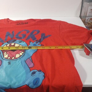 Puede incluir: Camiseta roja con un personaje azul Stitch de Lilo & Stitch. El personaje se muestra con la boca abierta y la palabra "Angry" est&aacute; impresa sobre el personaje.