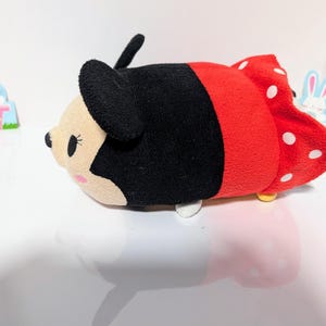 Peut inclure: Un jouet en peluche rouge et noir en forme de souris de dessin anim&eacute; avec des pois blancs. Le jouet a un nez noir, des yeux blancs et un n&oelig;ud noir.
