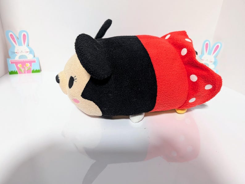 Peut inclure: Un jouet en peluche rouge et noir en forme de souris de dessin anim&eacute; avec des pois blancs. Le jouet a un nez noir, des yeux blancs et un n&oelig;ud noir.