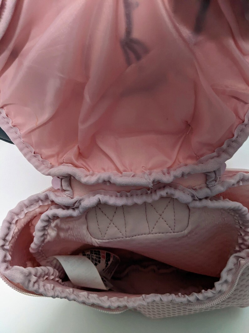 Op de afbeelding: Een roze trekkoordtas met een mesh voering. De tas is open en de voering is zichtbaar. De tas heeft een wit label met zwarte tekst.