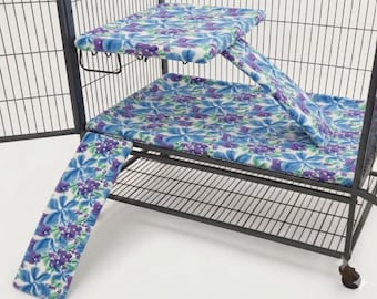 May include: A black metal pet cage featuring a multi-level interior with soft fabric covers. The covers have a white background with a repeating floral pattern in shades of blue and purple, including a rectangular platform, a base mat, and two ramps.