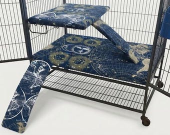 May include: A black metal pet cage featuring a dark blue fabric liner with a celestial map print, including a raised platform, a ramp, and a matching floor mat. A blue plastic food or water bowl is attached to the side of the wire enclosure.