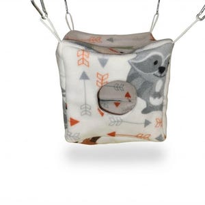 May include: A soft, cube-shaped hanging pet hammock made of white fleece fabric featuring a repeating pattern of gray and orange arrows and cartoon raccoons. The cube has a circular opening on the front side and is suspended by four white straps.