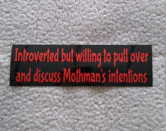 May include: Black and red bumper sticker with the text "Introverted but willing to pull over and discuss Mothman's intentions."