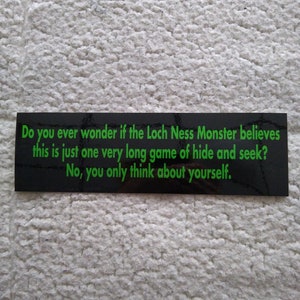 May include: Black and green sign with white text that reads: "Do you ever wonder if the Loch Ness Monster believes this is just one very long game of hide and seek? No, you only think about yourself."