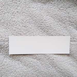 Puede incluir: Una pegatina rectangular blanca con una superficie lisa.