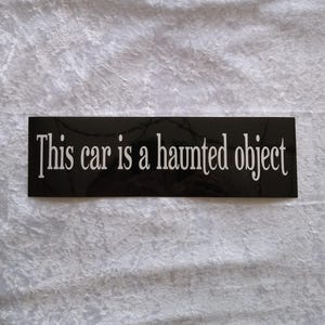 May include: Black and white sticker with the text "This car is a haunted object" printed on it.