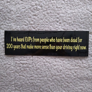May include: Black and yellow bumper sticker with the text "I've heard EVPs from people who have been dead for 200 years that make more sense than your driving right now."