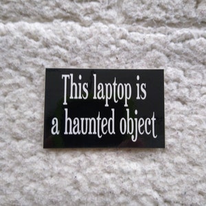 May include: A black sticker with white text that reads "This laptop is a haunted object."