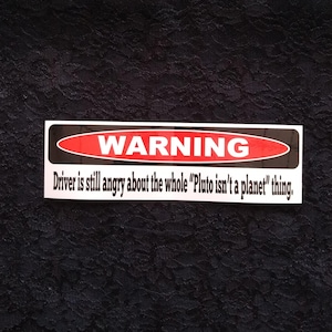 May include: A black and white warning sticker with red text that reads "WARNING" and the text "Driver is still angry about the whole "Pluto isn't a planet" thing."