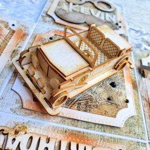 Op de afbeelding: Een gedetailleerd houten model van een oldtimer, met open zitplaatsen en gedetailleerde wielen. De lichtbruine auto staat op een decoratieve papieren achtergrond met een vintage ontwerp. Het beeld suggereert een handgemaakt item met een nostalgisch thema.