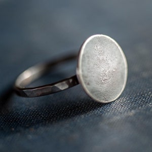 May include: A silver ring with a large, round, textured top. The ring band is hammered and has a matte finish.
